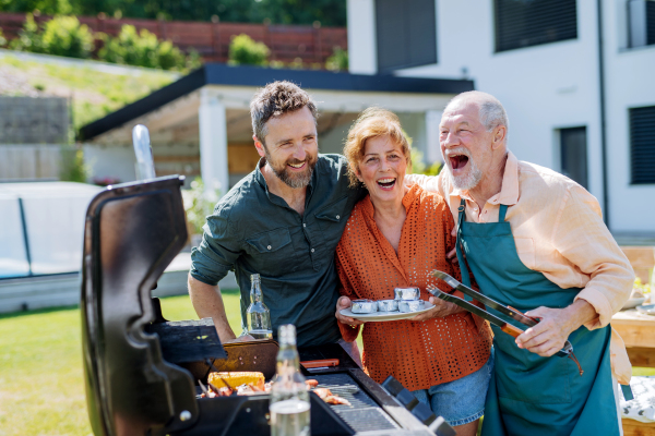 A senior couple with adult son grilling outside on backyard in summer family during garden party