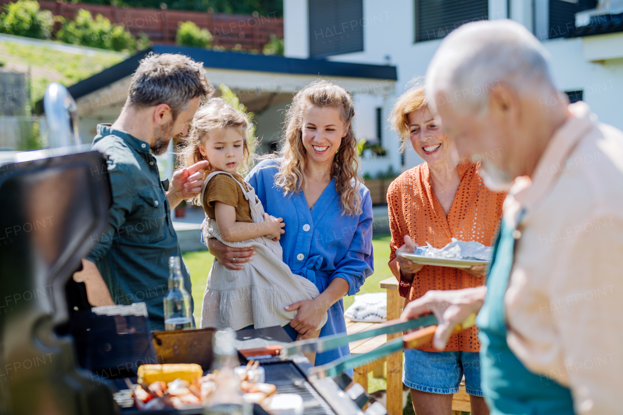 A multi generation family grilling outside on backyard in summer during garden party