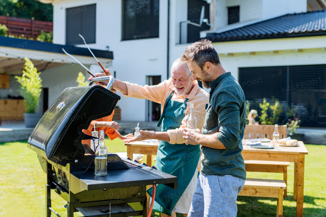 A senior father with adult son grilling outside on backyard in summer family during garden party