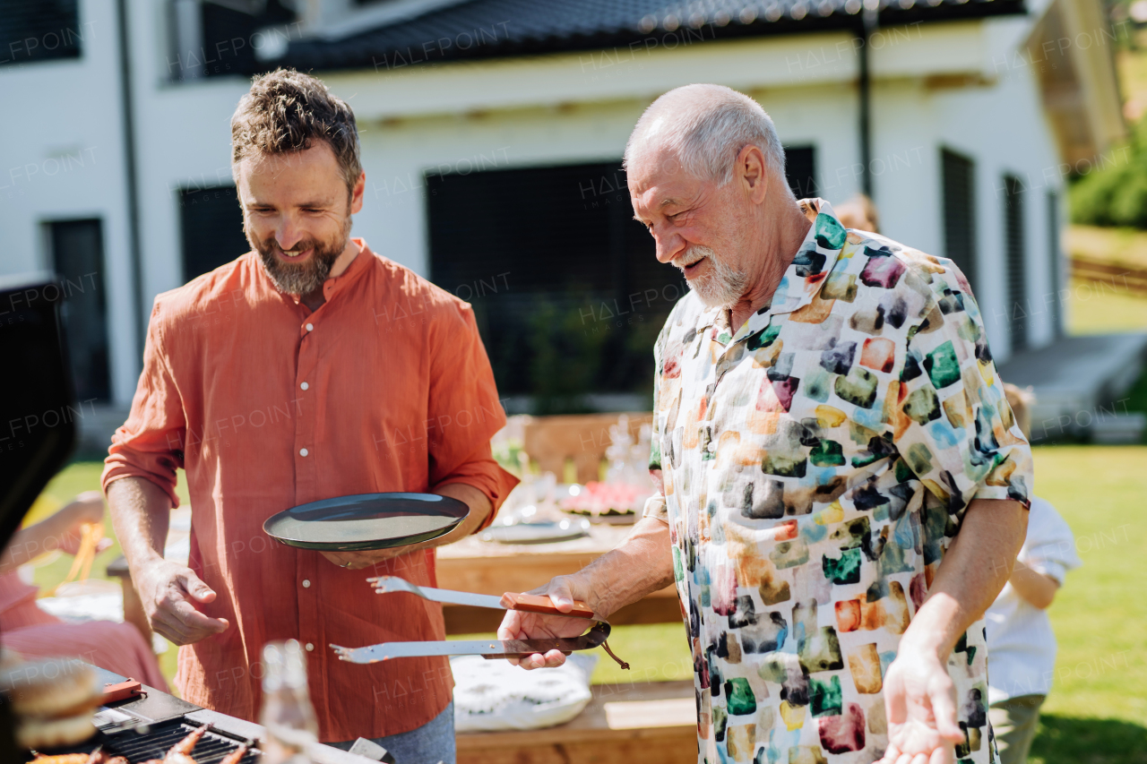 A senior father with adult son grilling outside on backyard in summer family during garden party