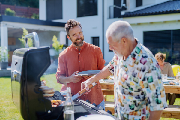 A senior father with adult son grilling outside on backyard in summer family during garden party