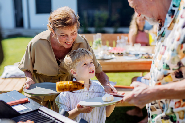 Grandparents serving grilled cheese and corn their grandson at garden grill party.