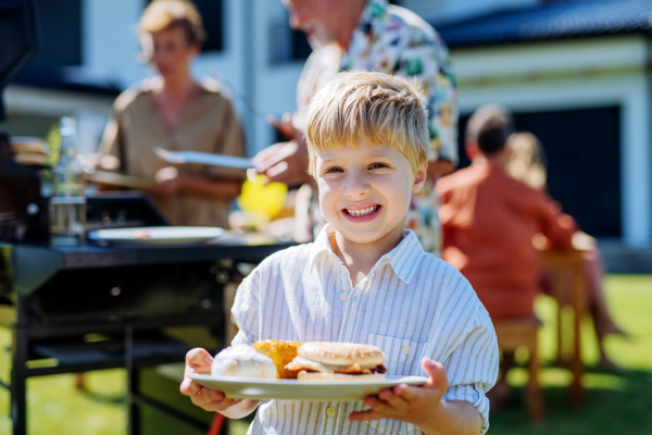 A happy little boy serving burgers at multi generation garden party in summer.