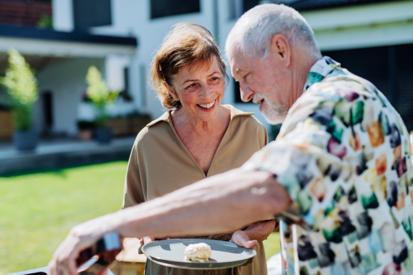 Senior man grilled outdoor at garden, giving his wife fresh hamburger.