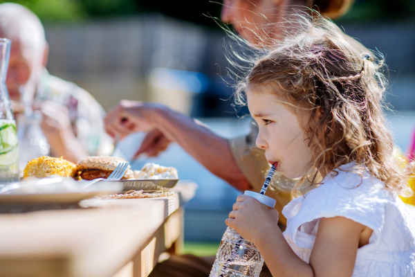 A family eating at barbecue party dinner in garden, little girl drinking water and enjoying it.