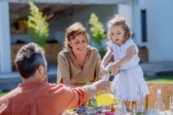 A multi generation family having garden party celebration, little girl is pouring juice to her father.