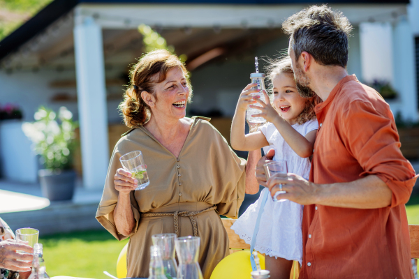 Multi generation family having garden party celebration, little girl with her dad and grandmother drinking a water with lemon, having nice time.