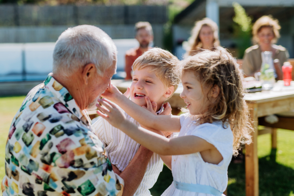 Little children having fun with their grandfather at outdoor bbq party.