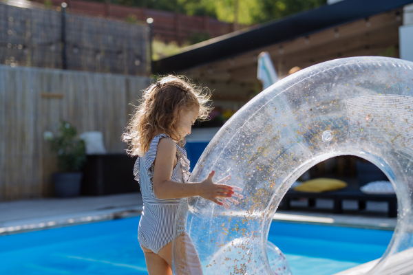 A happy kid having fun by swimming pool with inflatable ring. Summer outdoor water activity for kids.