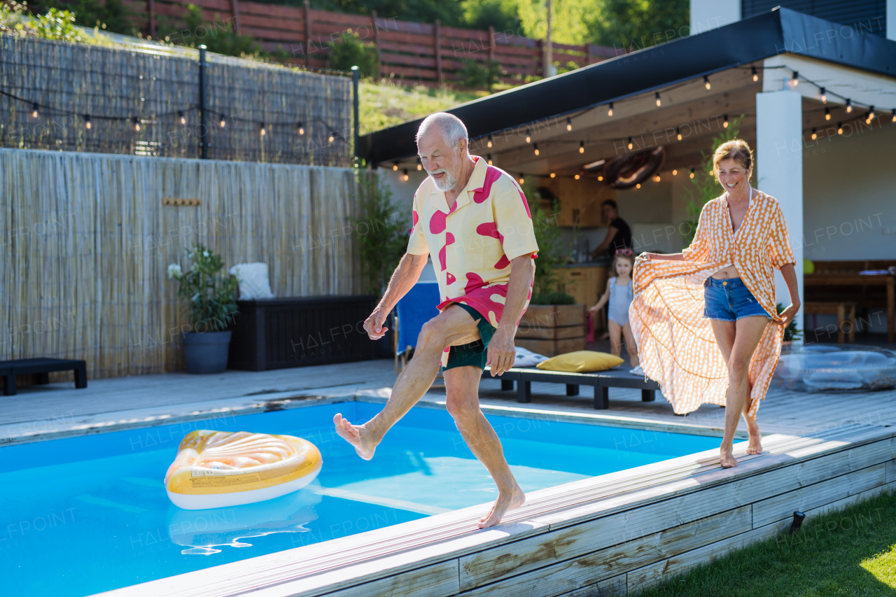 A happy senior couple having fun when walking by swimming pool during summer generation family holidays.