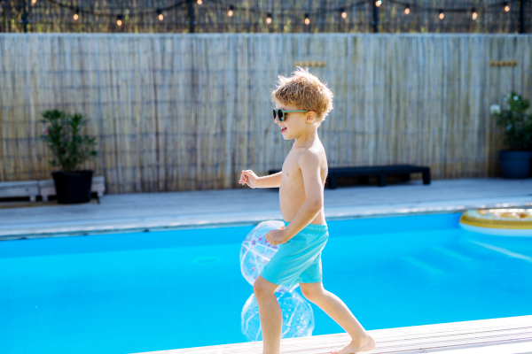 A happy kid having fun when running round the swimming pool with. Summer outdoor water activity for kids.