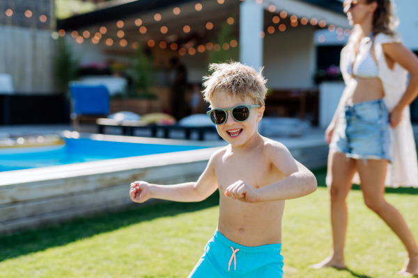 Little boy enjoying summer time with his mother on their backyard with swimming pool.