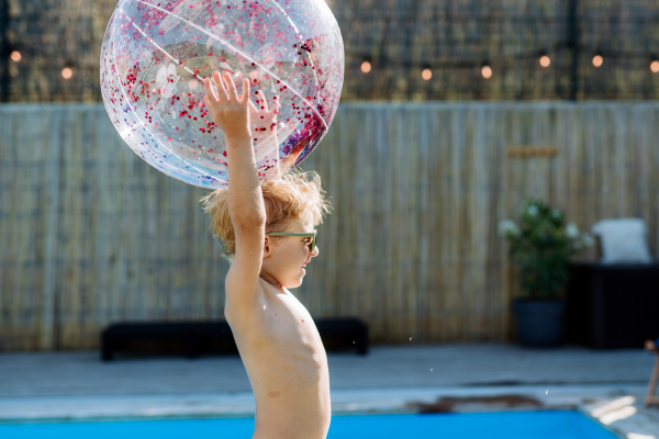 Little boy playing with inflatable ball near their swimming pool on a backyard.