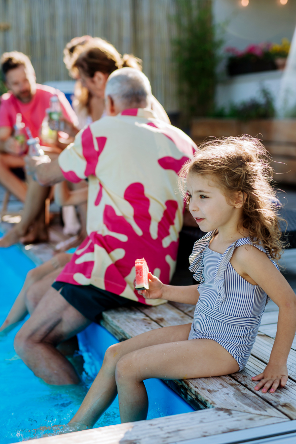 A multi generation family enjoying summer time and sitting at backyard pool.