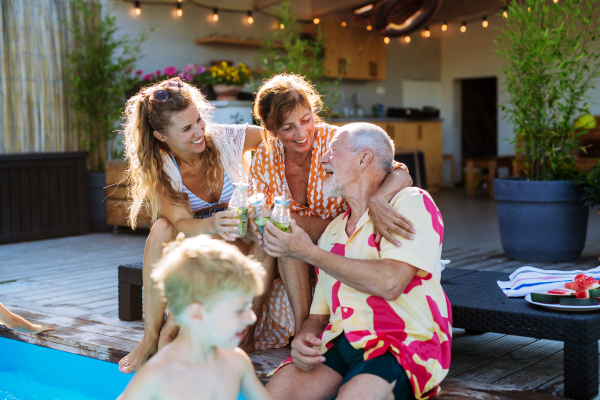 A multi generation family enjoying drinks when sitting at backyard pool.