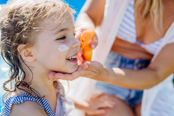 A close-up of young mother applying and sunscreen lotion to her daughter. People skin protection. Safety sunbathing in hot day.