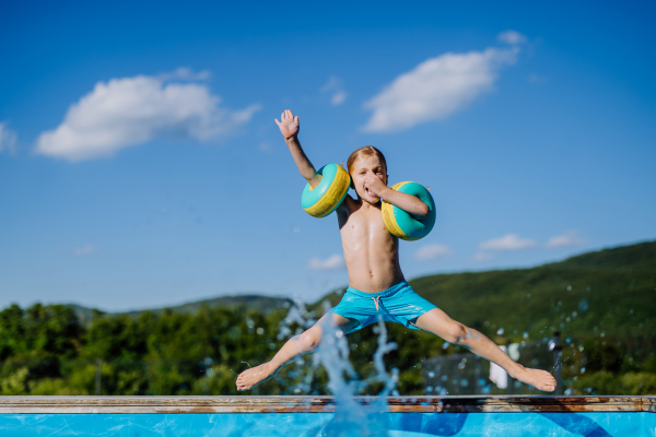 A hjappy kid having fun when jumping to swimming pool with inflatable armbands. Summer outdoor water activity for kids.