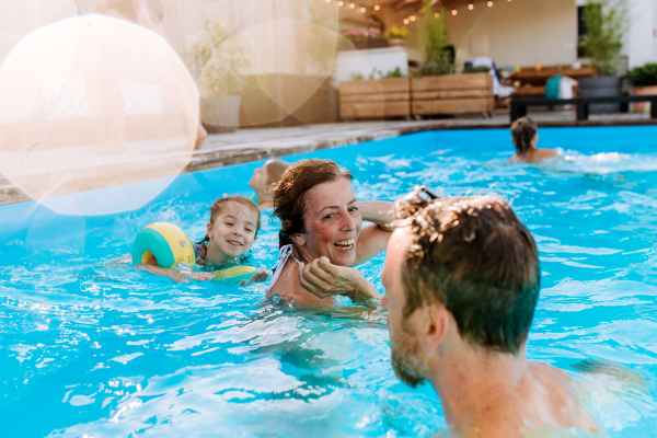 A multi generation family having fun and enjoying swimming in backyard pool.