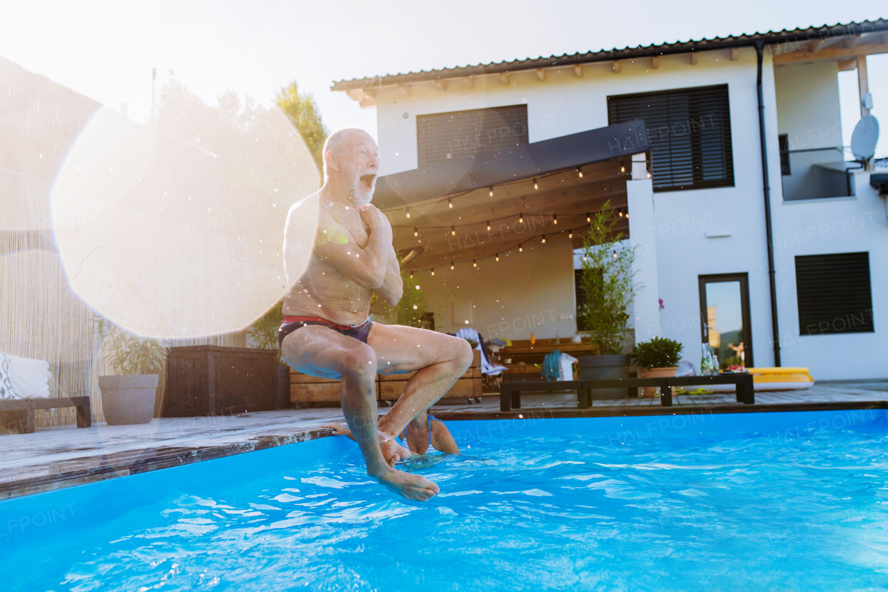 Happy senior man jumping into a swimming pool at backyard.