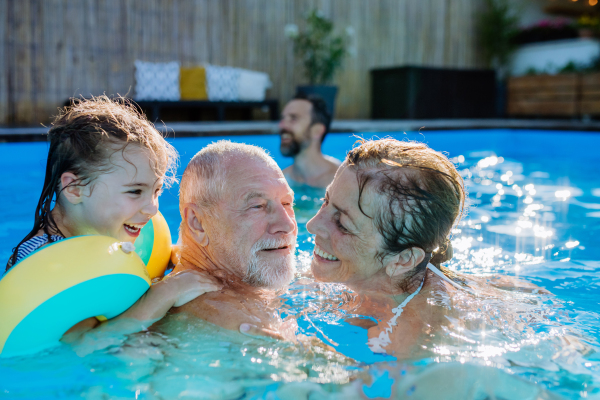 A multi generation family having fun and enjoying swimming in backyard pool.