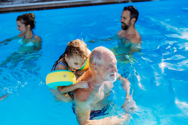 A multi generation family having fun and enjoying swimming in backyard pool.