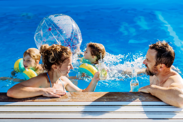 Happy young family with two kids spending summer time together in a pool.