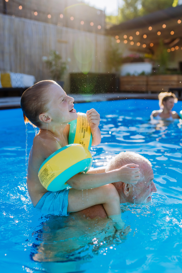 A grandfather with his granson having fun together when playing in the swimming pool at backyard.