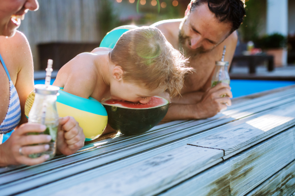 Young family enjoying summer time in a swimming pool, having drinks and watermelon.