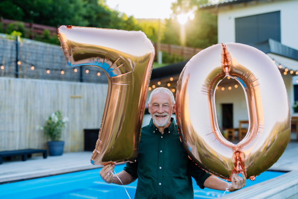 A man with number 70 balloons celebrating birthday near backyard pool.