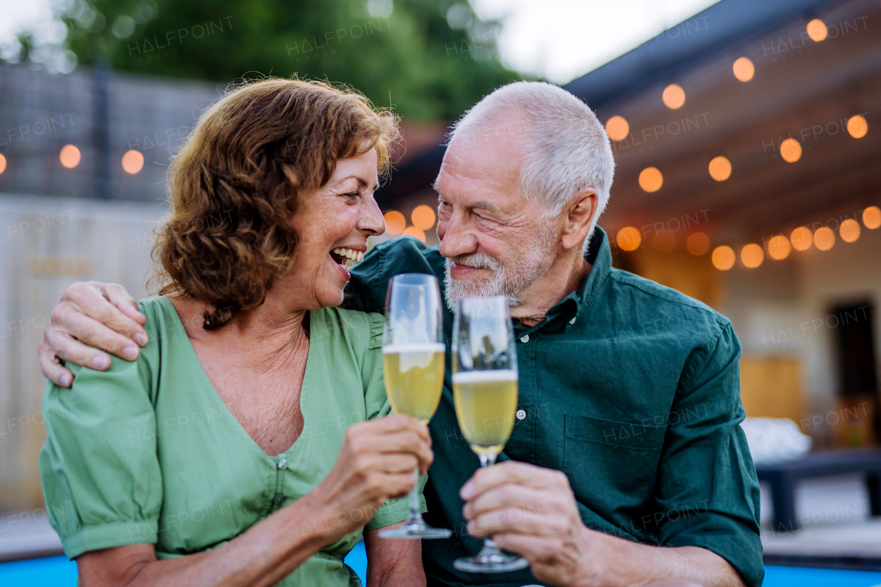 A man with number 70 balloons with his wife celebrating birthday and toasting with wine near backyard pool.