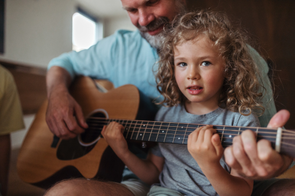 Father and daughter playing guitar together. Children learning play on musical instrument from parent.