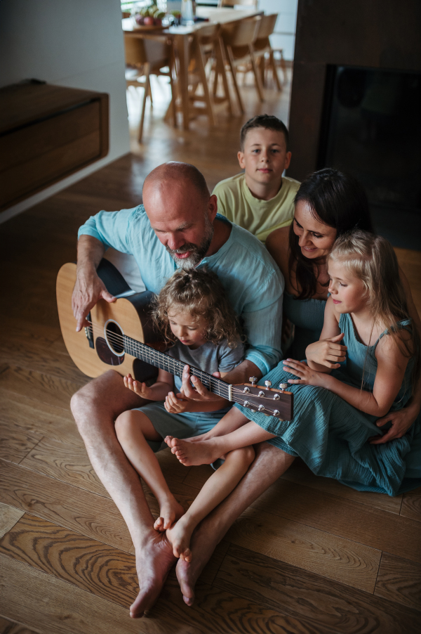 Father playing on guitar for his family. Family having fun and singing together. Concept of family bonding.