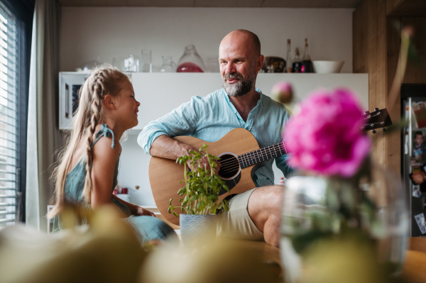 Father playing guitar for his cute daughter, girl singing. Children learning play on musical instrument from parent.