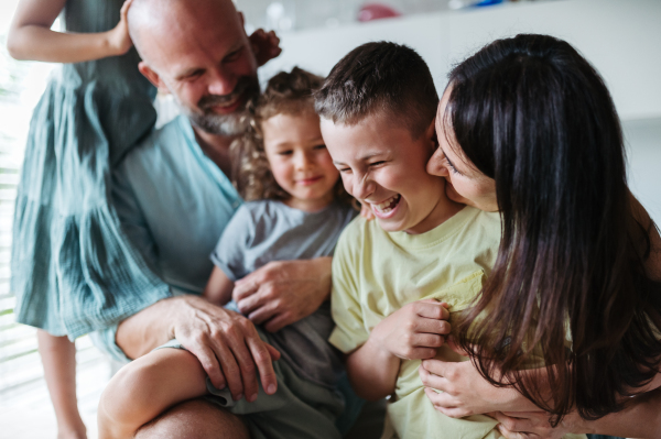 Cheerful family with three kids having fun together in kitchen. Mother kissing laughing son. Concept of family bonding.