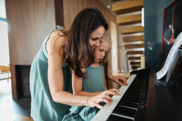 Mother and daughter playing on piano together. Children learning play on musical instrument from parent.