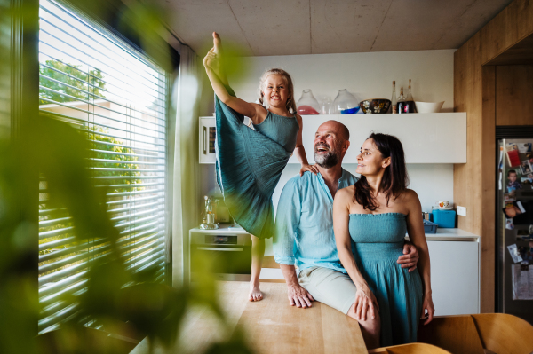 Little girl dancing on the kitchen countertop, while parents watching her. Cheerful family having fun together in kitchen. Little ballerina making funny face. Concept of family bonding.