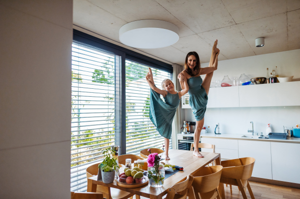 Little girl and mother dancing on the kitchen table as ballerinas. Mom and daughter having fun together in kitchen. Concept of Mother's Day.