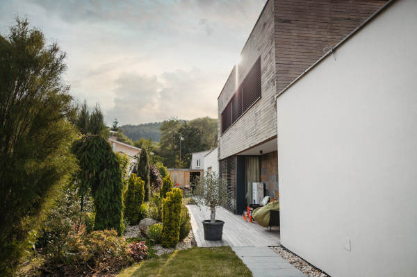 Modern house with beautifully landscaped home garden and wooden terrace deck, patio. Side, outdoor view of modern villa in the city.