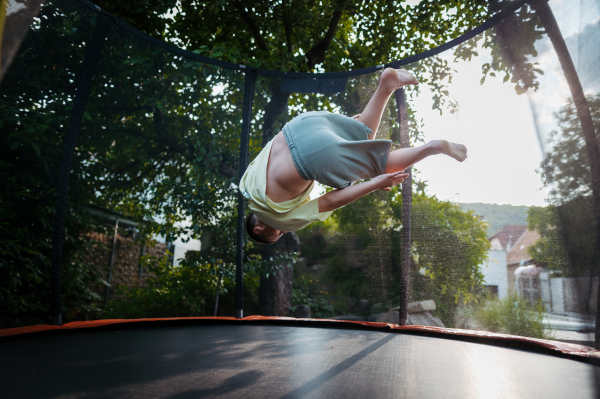 Little girl jumping on trampoline in the backyard, doing somersaults. Dangers and risks of trampoline for kids.