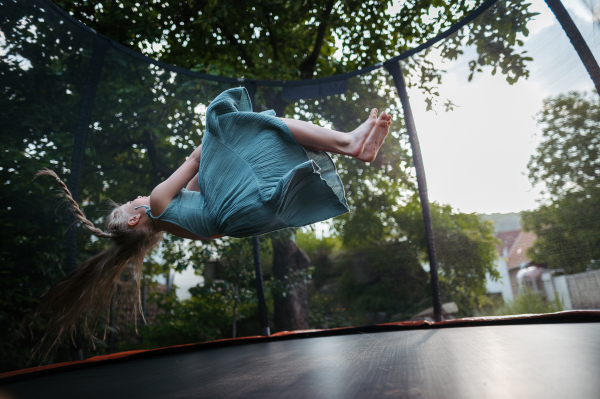 Little girl jumping on trampoline in the backyard, doing somersaults. Dangers and risks of trampoline for kids.