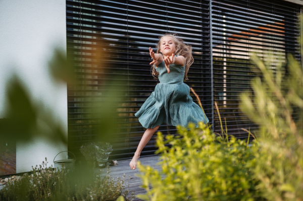 Little girl is dancing outside on the terrace of the house, jumping and having fun. Adorable young girl in summer dresses with blonde hair outside.