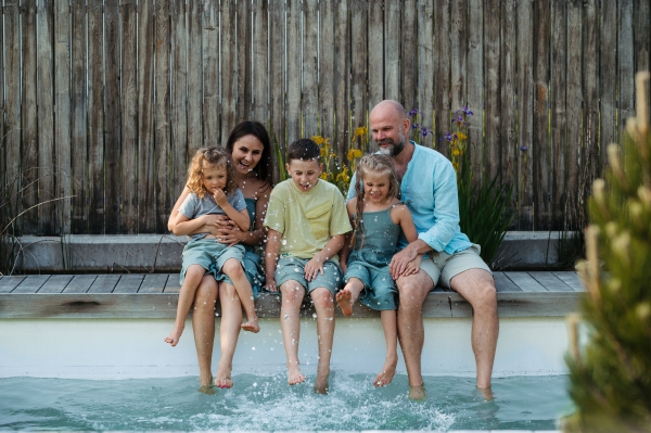 Cheerful family with three kids having fun together sitting by a pool, splashing water. Concept of family bonding.