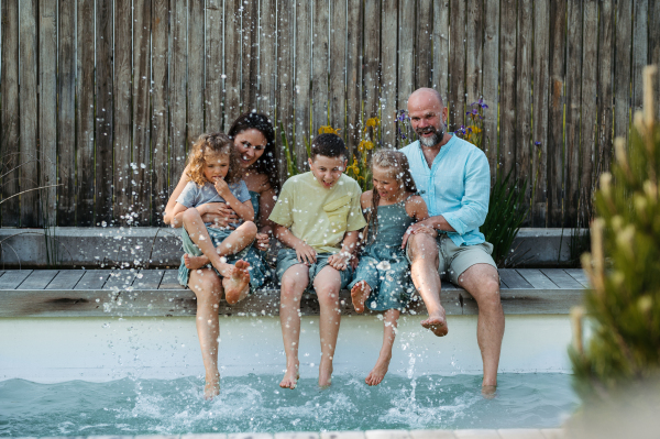 Cheerful family with three kids having fun together sitting by a pool, splashing water. Concept of family bonding.