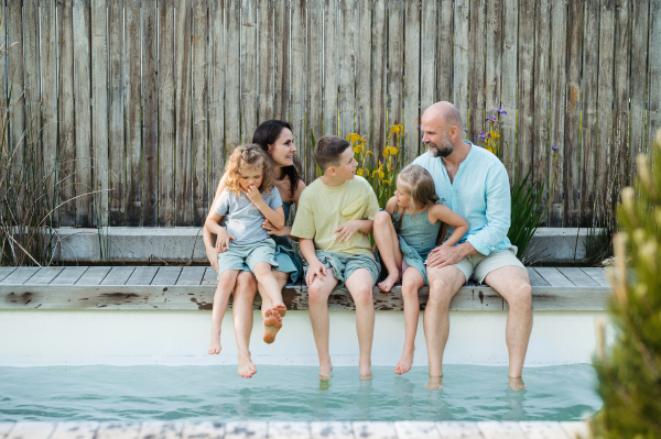 Cheerful family with three kids having fun together sitting by a pool, splashing water. Concept of family bonding.