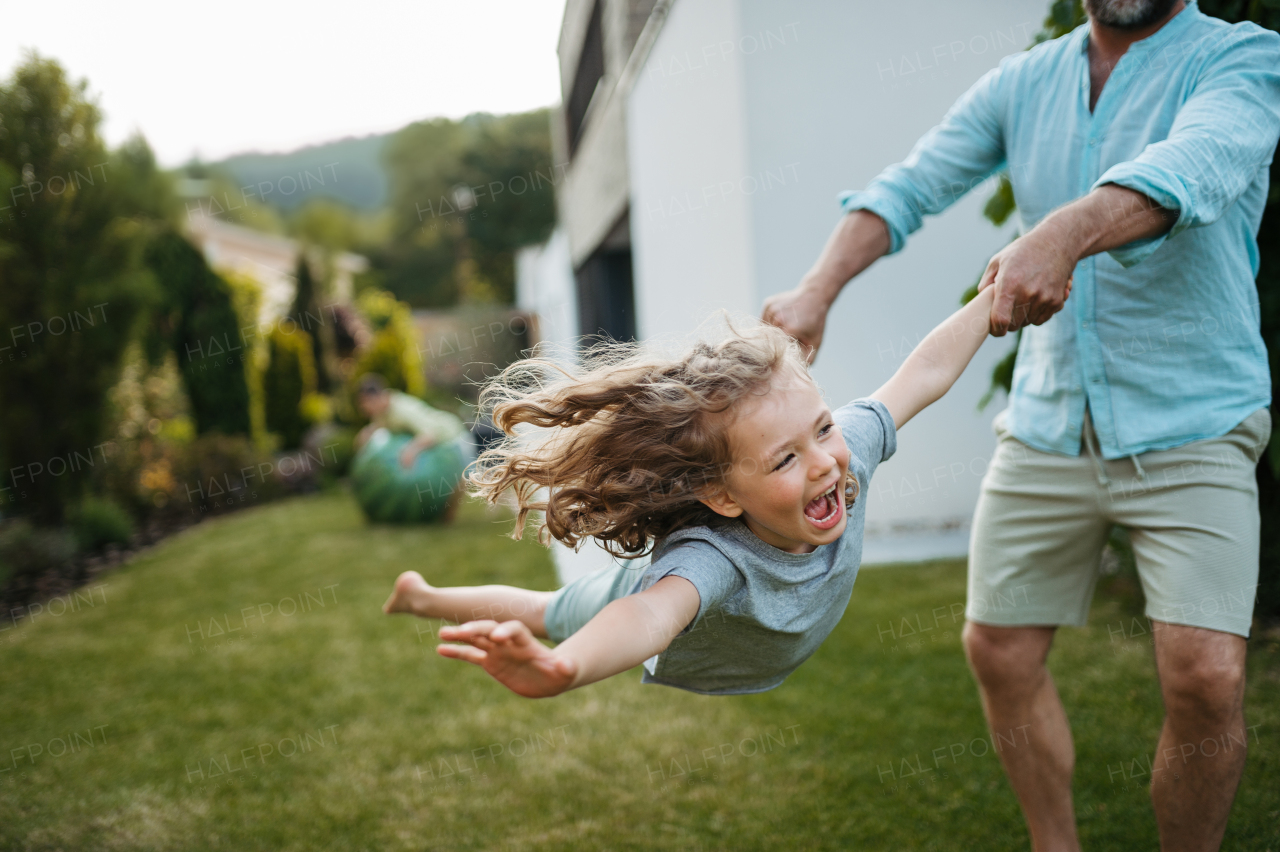 Father holding daugter and spinning her around in the garden. Dad with kid having fun outdoors.