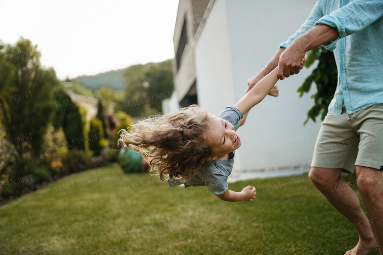 Father holding son and spinning he around in the garden. Dad with kid having fun outdoors.