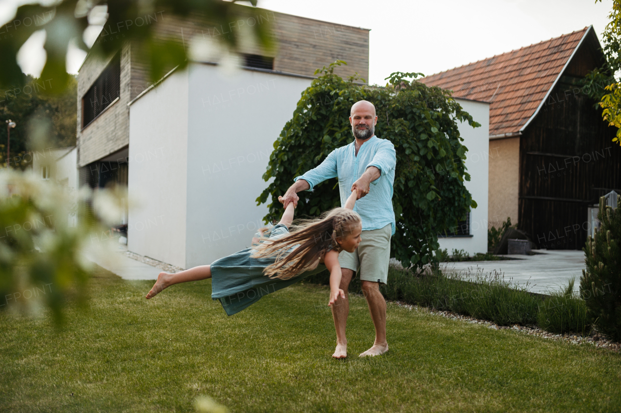 Father holding daugter and spinning her around in the garden. Dad with kid having fun outdoors. Father's day concept.