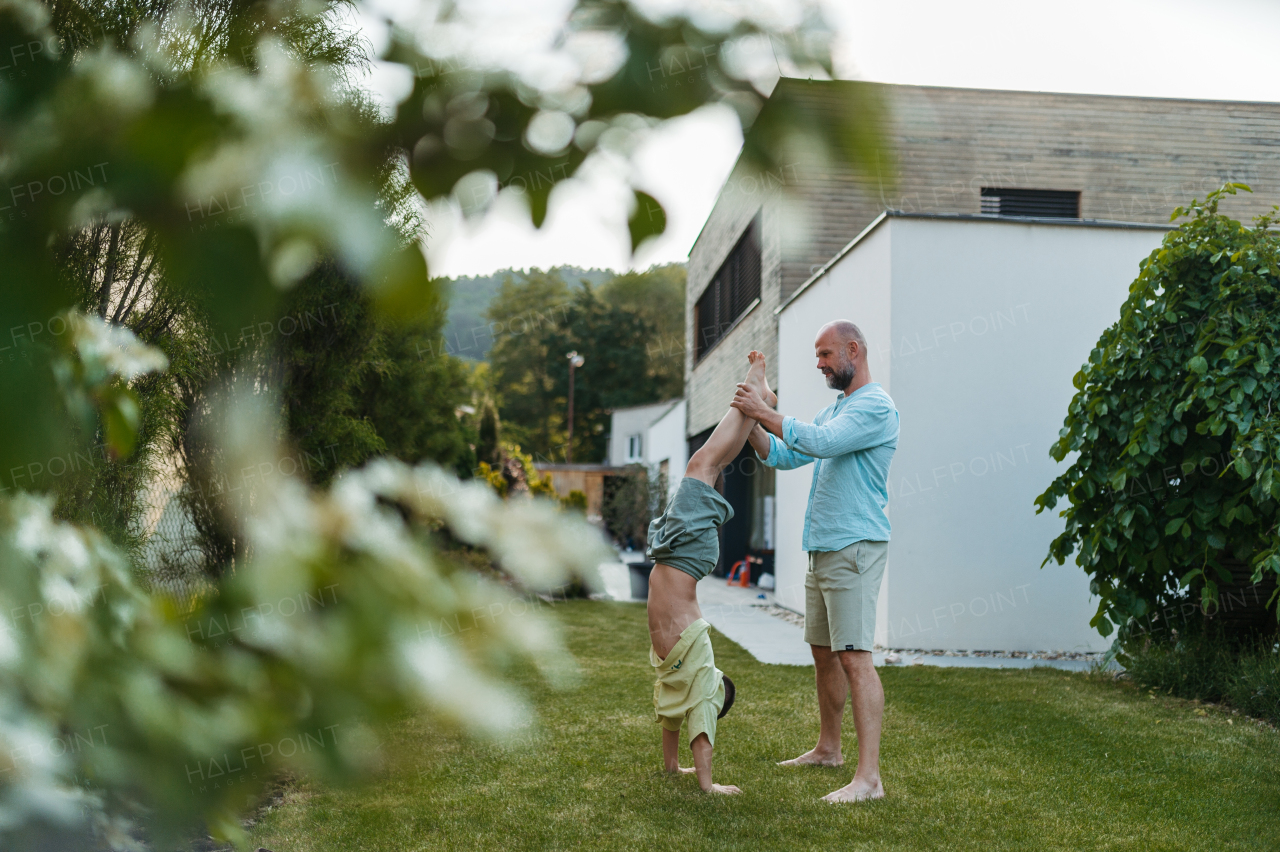 Father assisting his son as he does a handstand in the garden. Dad with kid having fun outdoors.