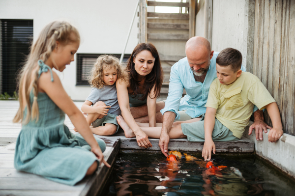 Cheerful family with three kids taking care of fish in pond. Koi fish in outdoor pond. Concept of family bonding.