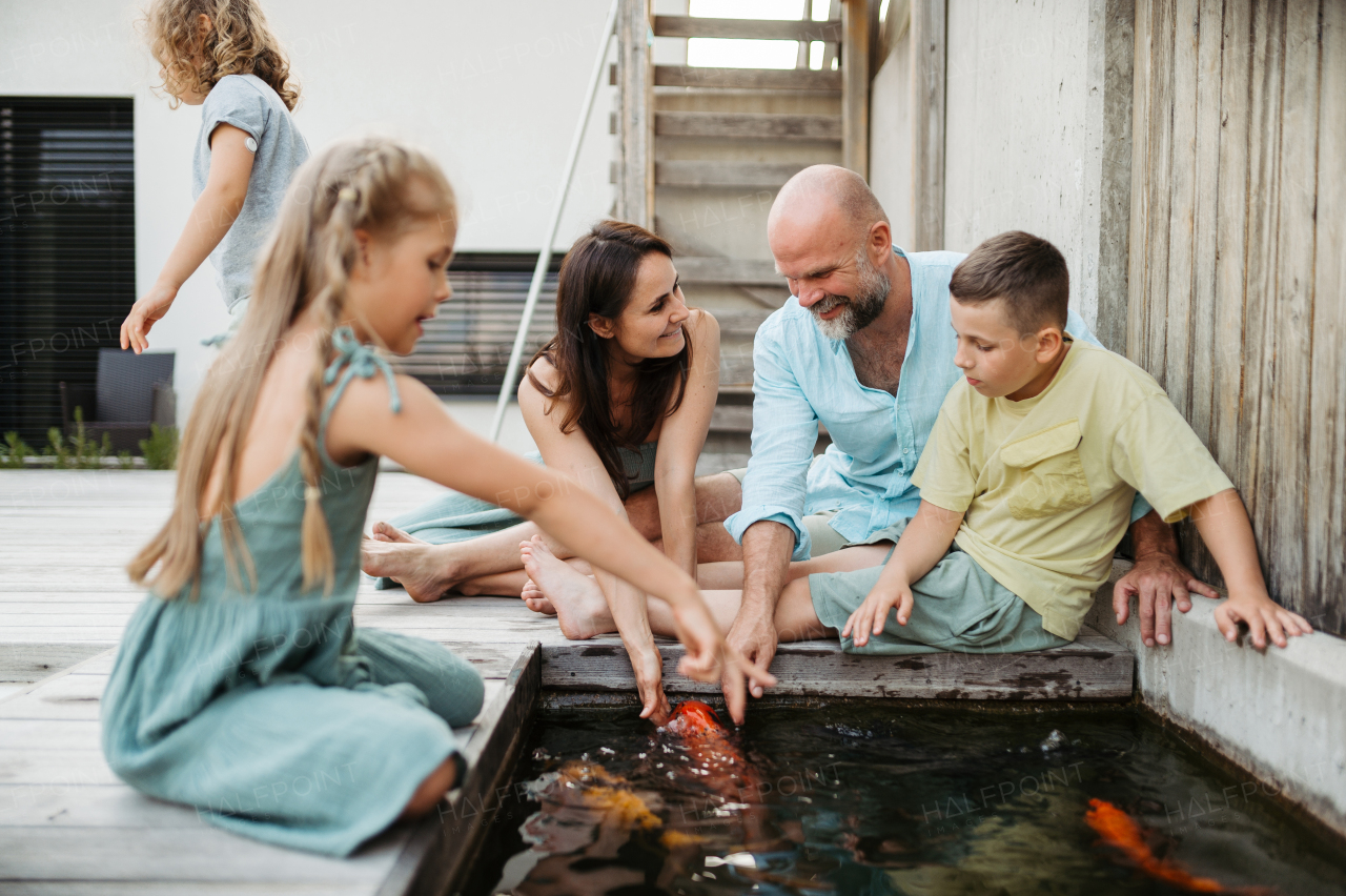 Cheerful family with three kids taking care of fish in pond. Koi fish in outdoor pond. Concept of family bonding.